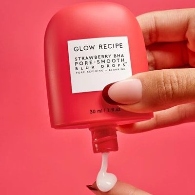 A hand squeezing a red bottle of Strawberry BHA Pore-Smooth Blur Drops
