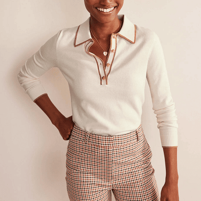 woman wears ivory merino polo sweater; the placket and collar are edged in a darker beige