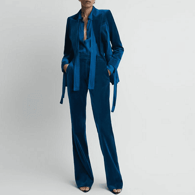 woman wears monotone outfit in a dark but bright blue velvet; she is wearing an untied pussybow blouse so it looks like a scarf around her neck; there are also untied long ties at the wrists. She's wearing sandals, sigh.