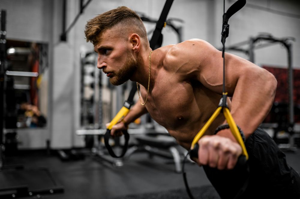 a man using TRX arm bands, demonstrating suspended bodyweight exercises for an effective upper body workout with a focus on arms, shoulders, and core strength