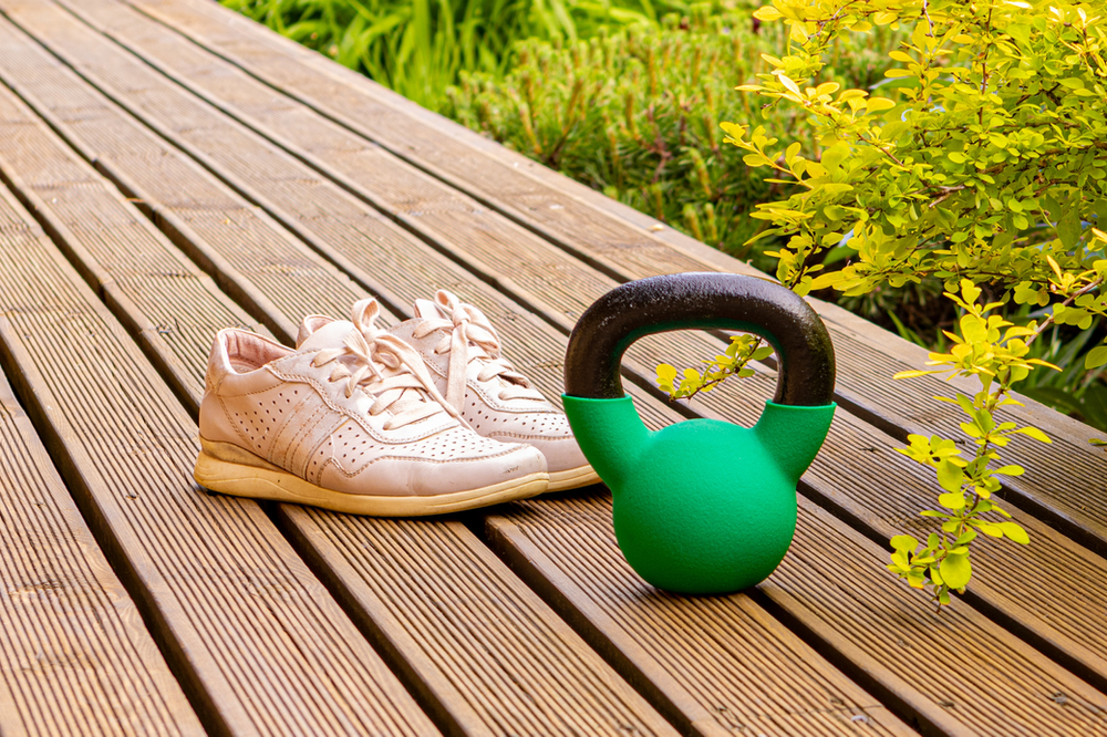 A single kettlebell placed beside a workout towel and pair of shoes on a gym floor, illustrating fitness essentials for strength training and exercise routines