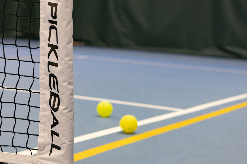 A colorful outdoor pickleball court with vibrant blue and green playing surface under bright sunlight, featuring net and boundary lines – an inviting and active space for pickleball enthusiasts to enjoy the game in the open air