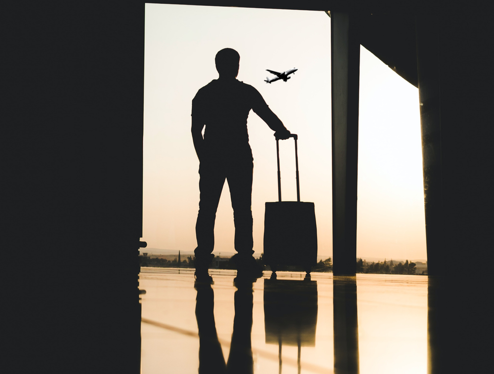 A man standing at a gate with bike luggage, illustrating the importance of durable and protective bike cases for air travel. The image showcases a traveler prepared for a cycling adventure, emphasizing the need for reliable luggage to safeguard the bicycle during transit.
