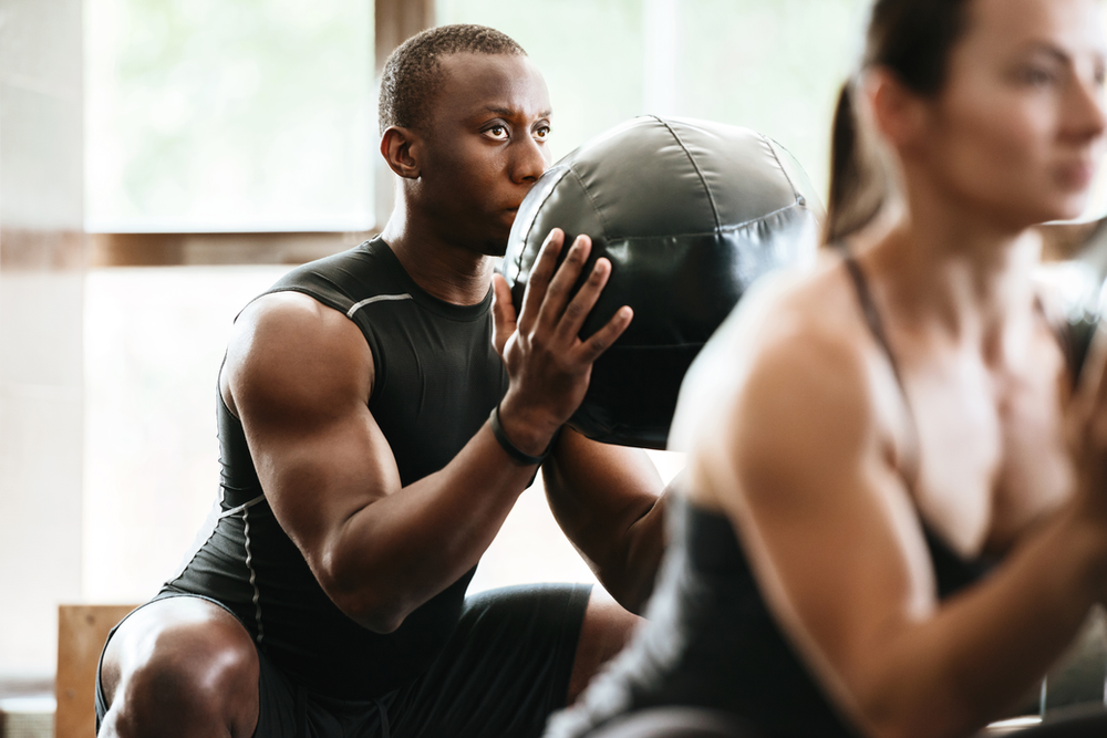 A man and woman sitting on the ground engaged in a fitness routine, incorporating a medicine ball into their exercises