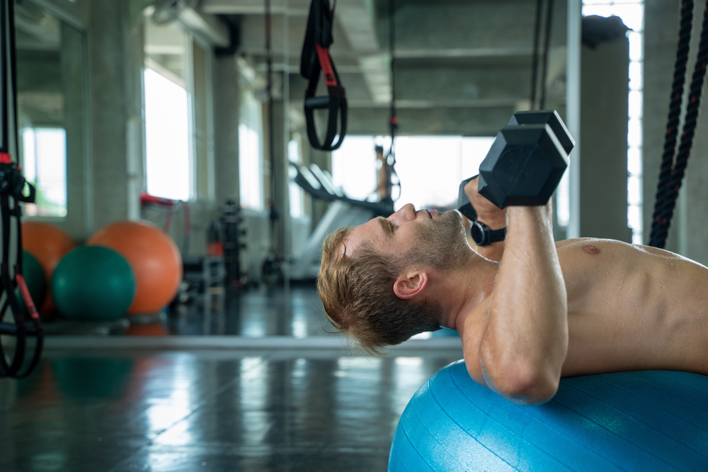 Man lifting handweights in a fitness setting. Strength training with dumbbells. Demonstrating dedication to exercise and health. Gym environment with workout equipment in the background