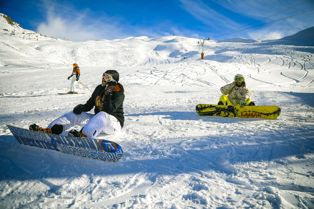Two beginner snowboarders in winter gear, standing in the snow with snowboards, excitedly preparing to embark on their snowboarding journey. The image captures the enthusiasm and camaraderie of individuals new to the sport, ready to learn and enjoy the snowy slopes together