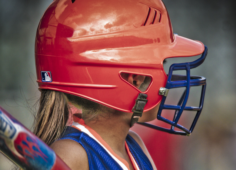 A young girl confidently wears a baseball helmet, ready for action on the field, showcasing a commitment to safety in sports