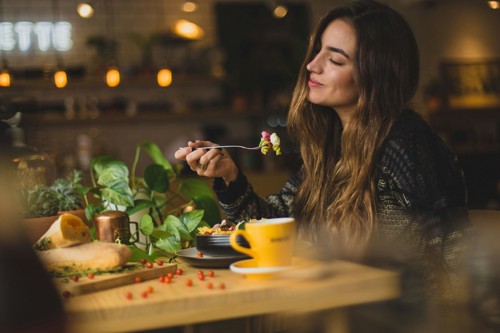  a woman sitting at a dining table, enjoying a well-balanced meal within her macros. The plate features a portion of grilled salmon (protein), a serving of quinoa (carbohydrates), and a variety of colorful vegetables. The woman is mindful of her nutrition, showcasing a healthy and balanced approach to eating in alignment with her macronutrient goals